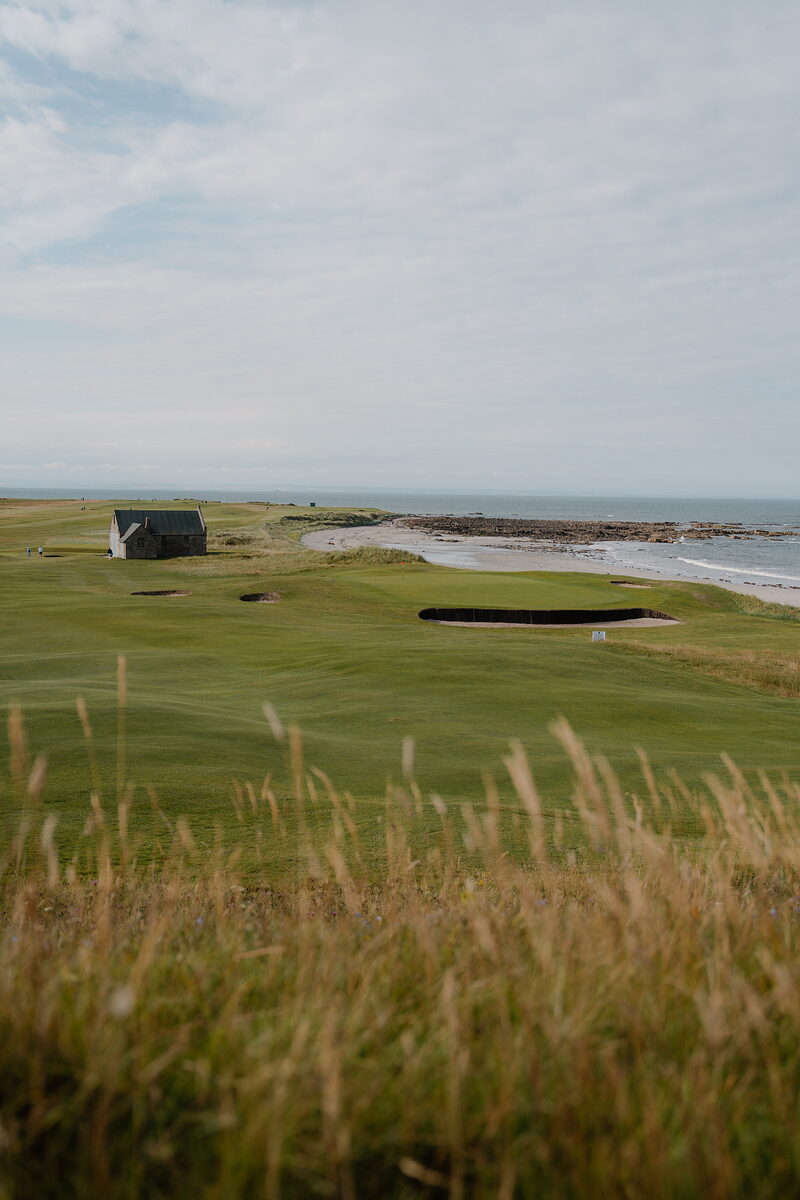A stone shelter beside the green at Crail, bunkers and a sandy shoreline stretching along the coast