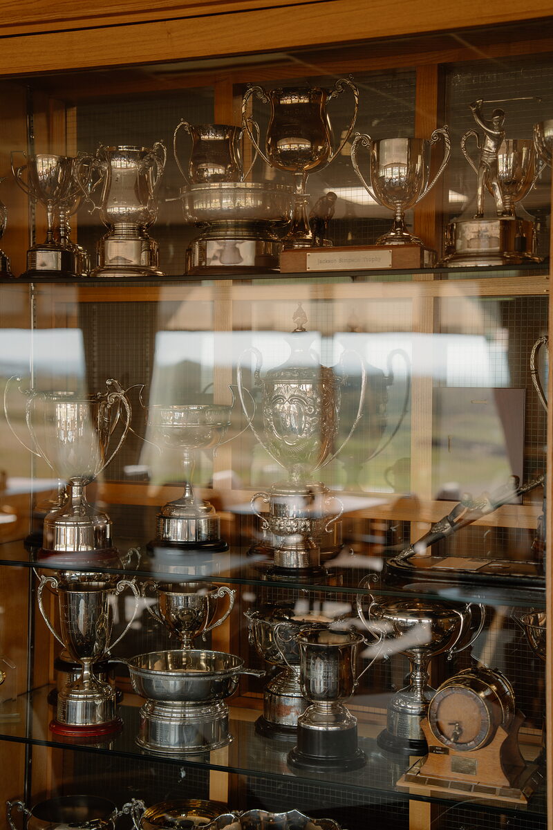 A glass display cabinet crowded with silver golf trophies and cups