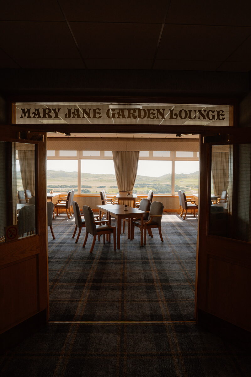 The Mary Jane Garden Lounge sign above an open doorway leading to a tartan-carpeted room with tables overlooking the links