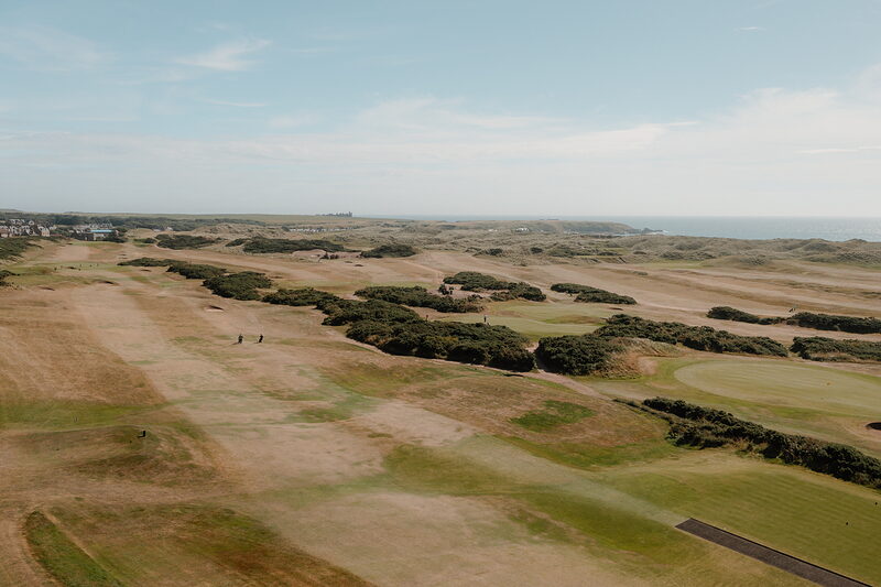Rolling dune fairways stretching towards the sea on a links course, golfers visible in the distance