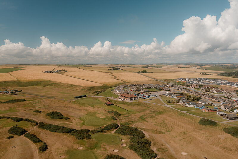 Farmland and a housing estate bordering a links course fairway seen from above