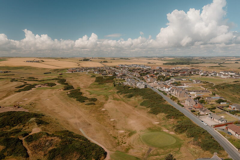 A village and golden fairways bordering farmland, roads winding between the houses