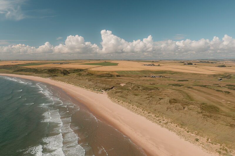 A long sandy beach curving along the coastline, farmland and dune links stretching inland