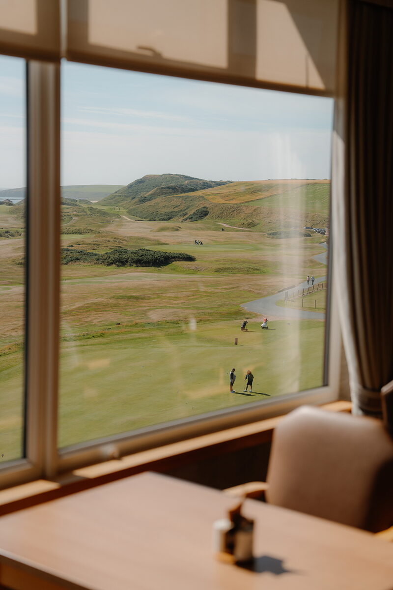 Golfers walking a path through dunes towards a green, a hill rising beyond the fairway