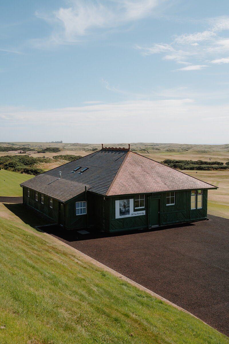 A dark timber clubhouse with a decorative ridge standing among dunes and open fairways