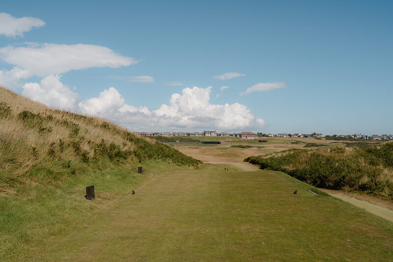 A fairway running towards a distant town, marker posts set along its edge
