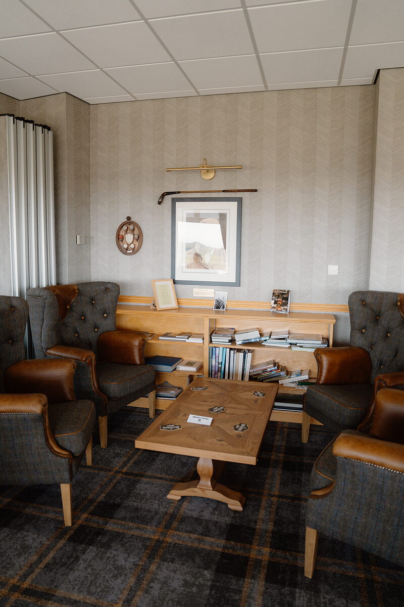 Leather armchairs arranged around a wooden coffee table beneath a framed landscape print and mounted golf club