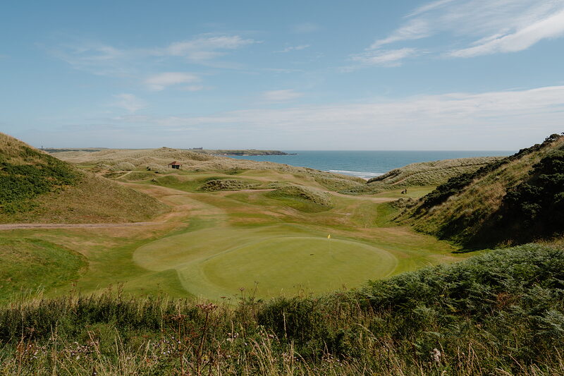 A green set among dunes with the sea and a rocky headland stretching behind