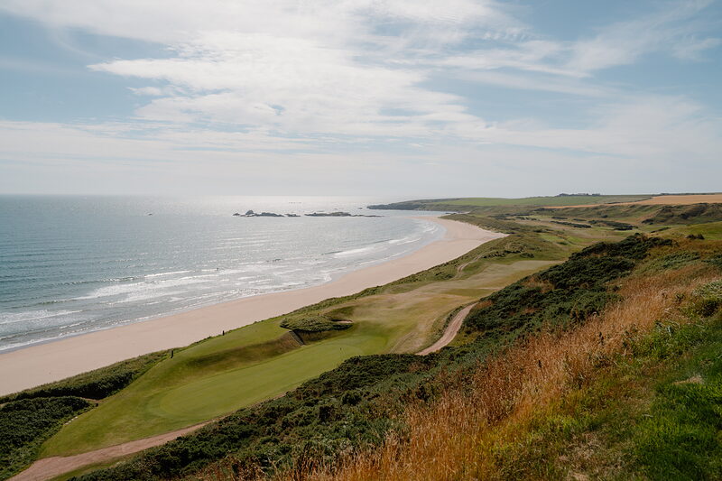 A green set among dunes overlooking a curving sandy beach and the sea