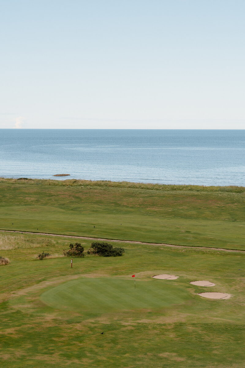 A golf green with bunkers overlooking the sea, a red flag marking the hole