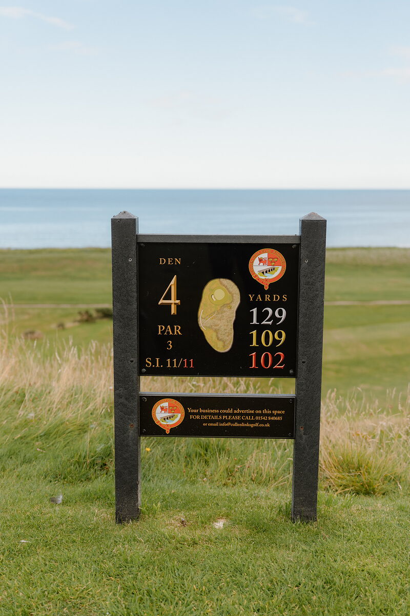 A tee marker sign for the Den, hole 4, par 3, overlooking the sea and fairway