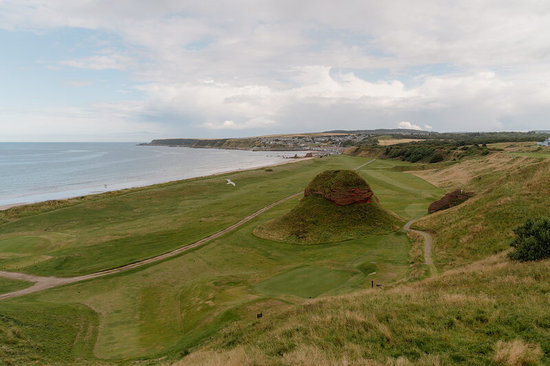 A red sandstone sea stack rising from a fairway beside a sandy beach and the sea