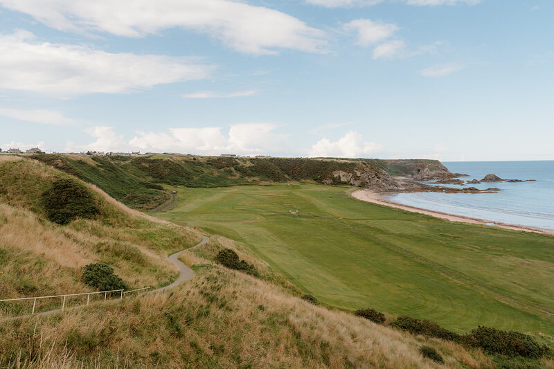 A fairway curving along cliffs above a sandy cove and the sea