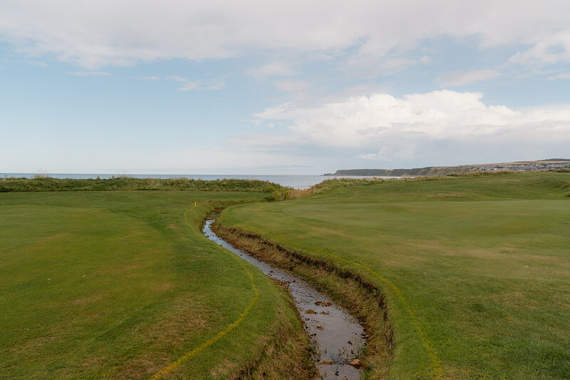 A stream winding through a fairway towards the sea and distant cliffs