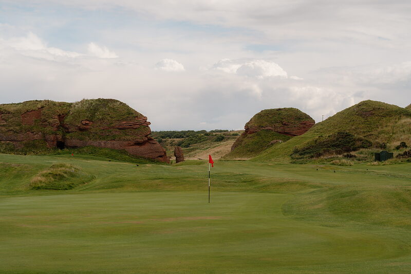 A flag marking a green set between two red sandstone outcrops