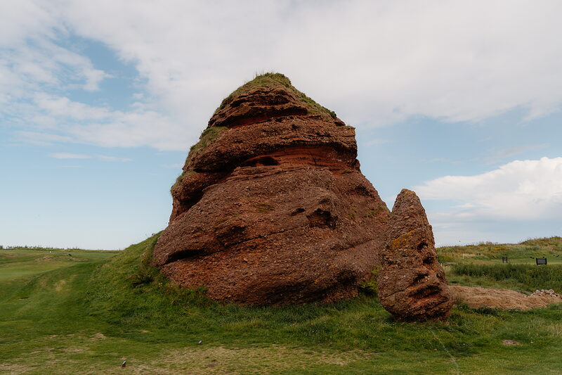 A weathered red sandstone stack rising from a grassy dune beside the fairway