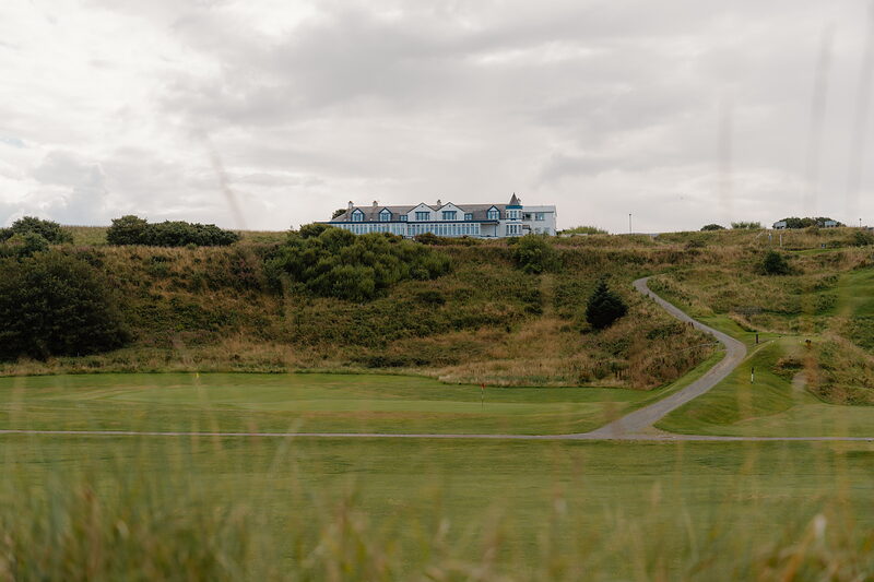 A pale blue clubhouse standing on a rise above a path curving through the fairway