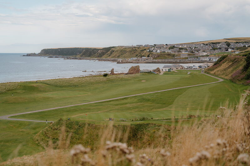 A fairway winding towards a hillside town, a rock stack rising from the beach below