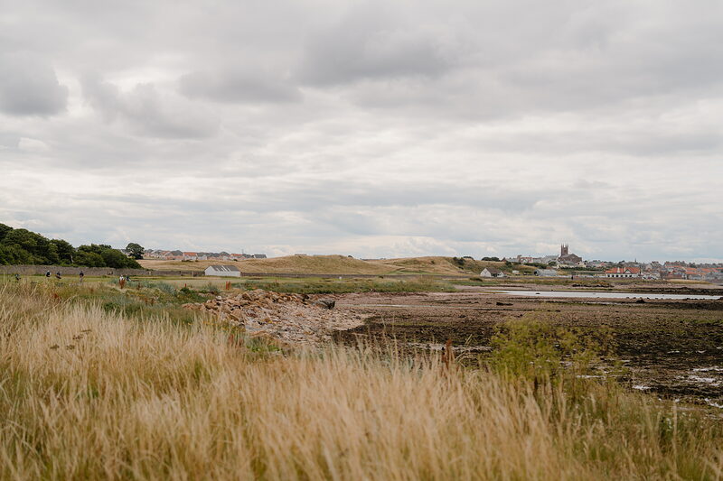Marshy grassland stretches toward a coastal town with a church spire in the distance.