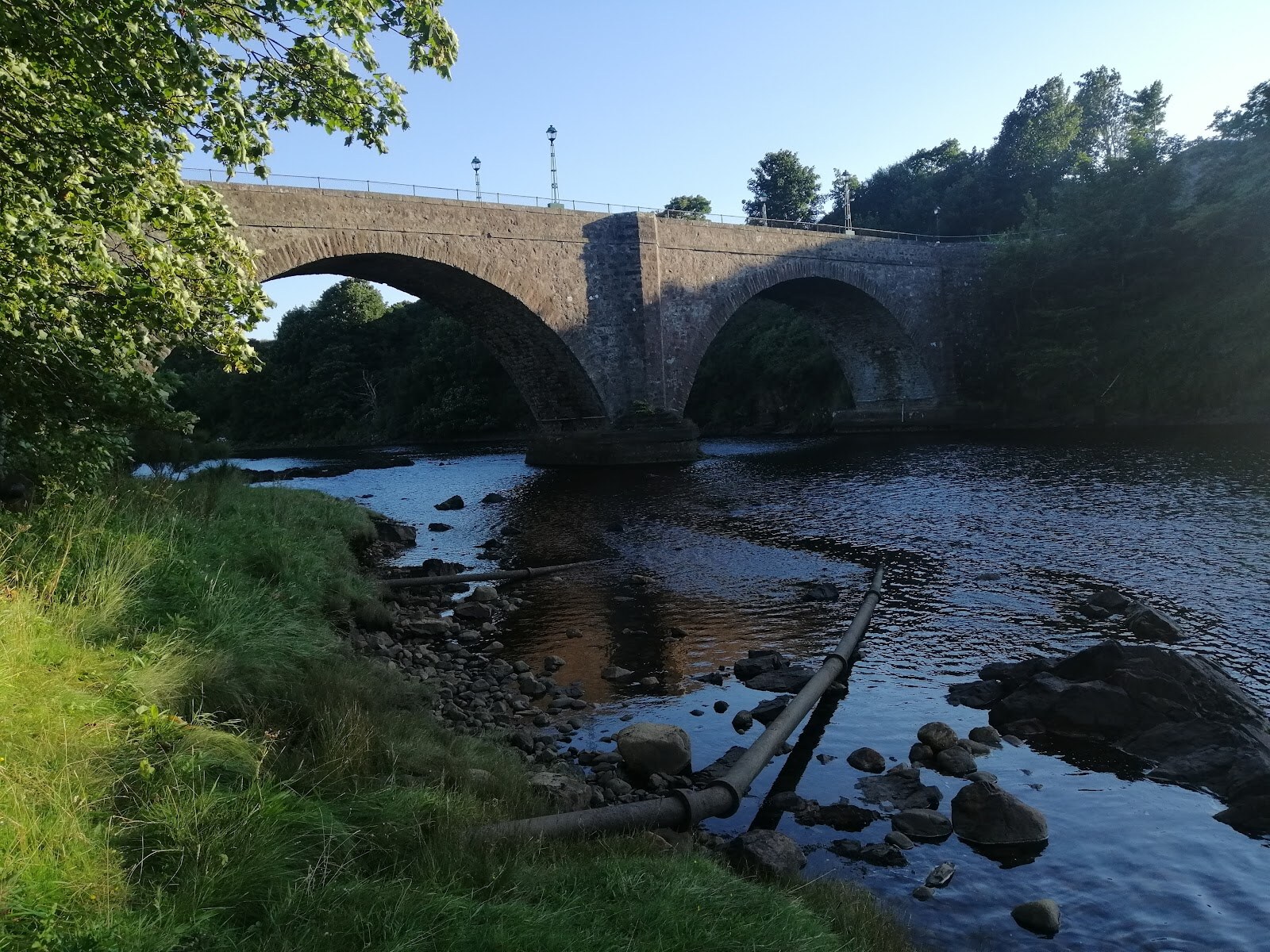 The arched stone bridge over the River Helmsdale, seen from the riverbank in evening light.