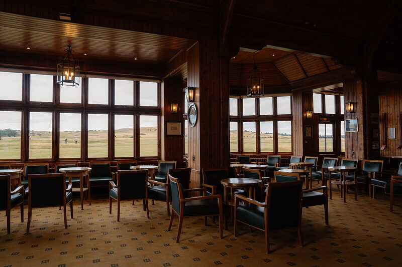 A wood-panelled golf clubhouse lounge with leather chairs facing tall windows over the links