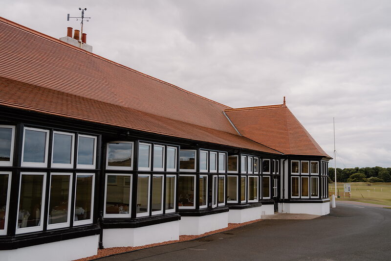 A black-and-white timbered clubhouse with a red tiled roof and bay windows along its length