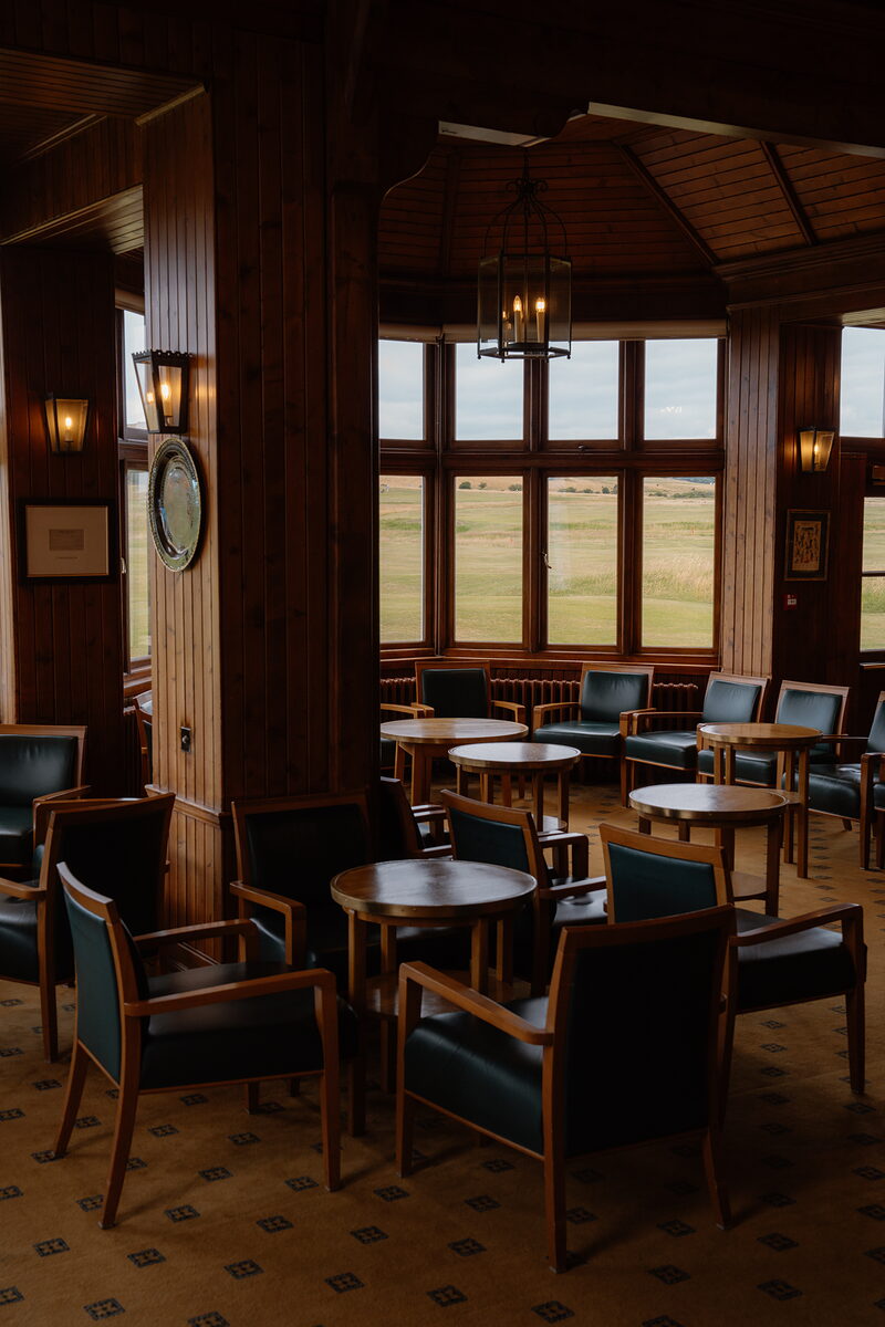 A wood-panelled lounge with leather armchairs and round tables beneath a domed ceiling, windows overlooking the links