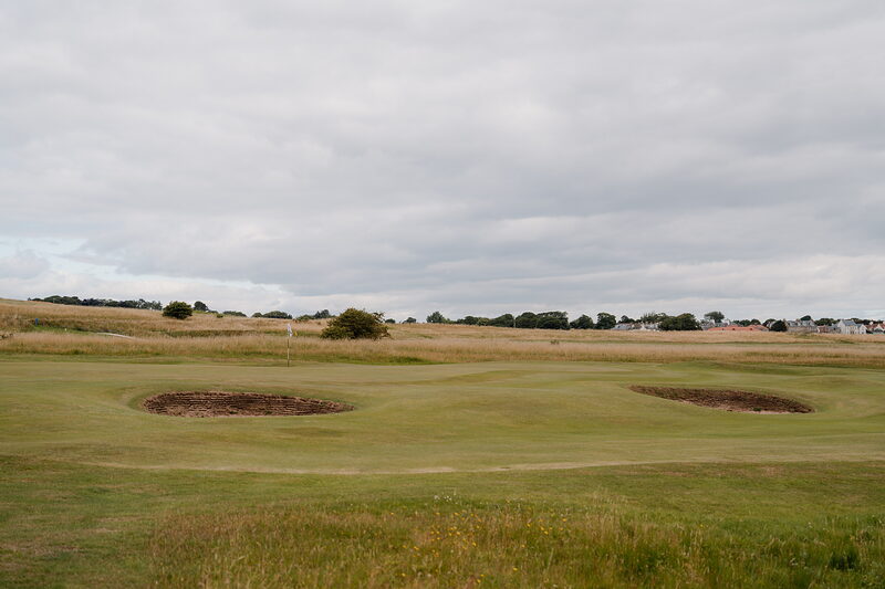 Twin bunkers flanking a fairway, a village visible on the horizon beyond a solitary tree