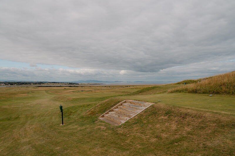 A grass-roofed bunker set into a fairway, a firth and distant hills stretching along the horizon