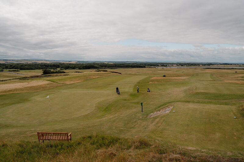 Golfers with buggies gathered on a green, a wooden bench set at the edge of the fairway
