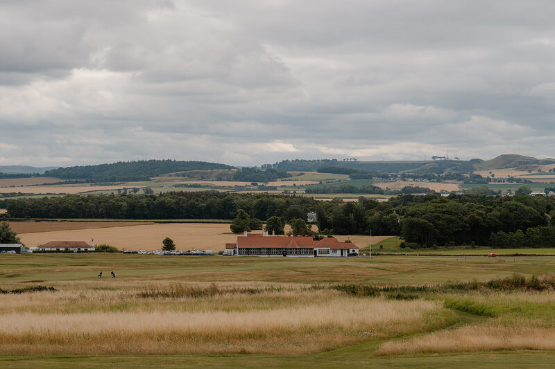 A fairway leading towards a clubhouse, farmland and wooded hills stretching to the horizon