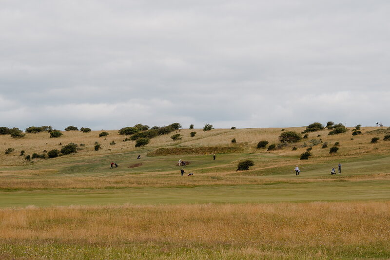 Golfers crossing a hollow between gorse-covered mounds on a fairway
