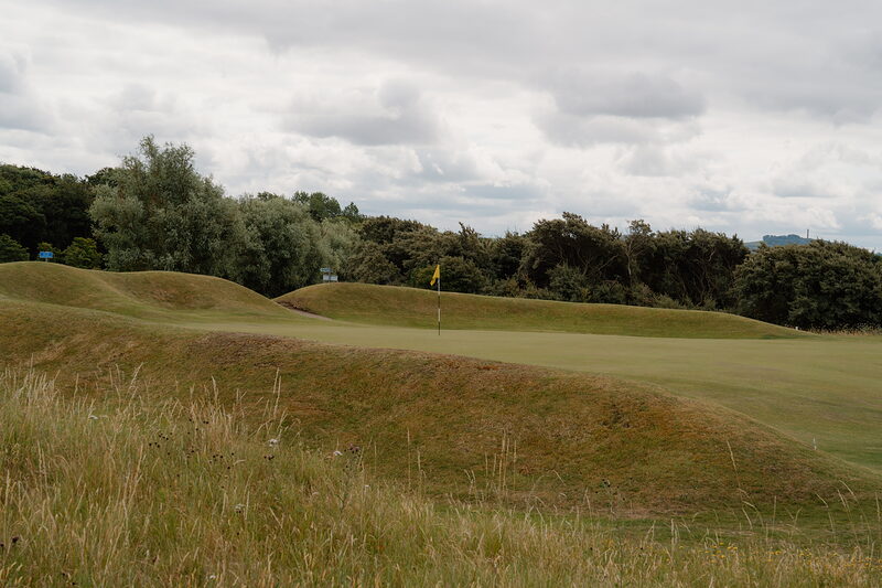 A yellow flag marking a green set among mounded fairway bordered by woodland