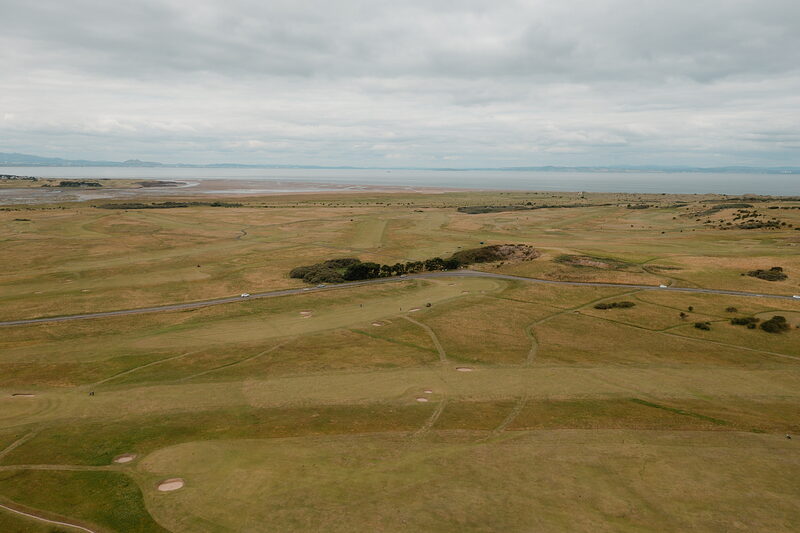 A fairway crossed by paths leading towards a distant firth and hills