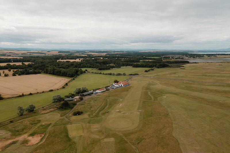 A fairway leading towards farm buildings and hedgerows stretching to the horizon