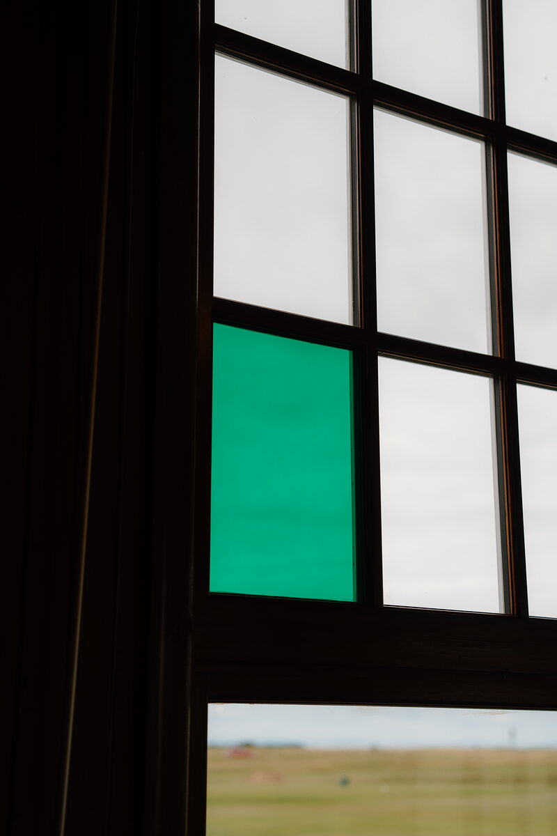 A green pane of glass reflecting light within a paned window, fields visible through the lower panel