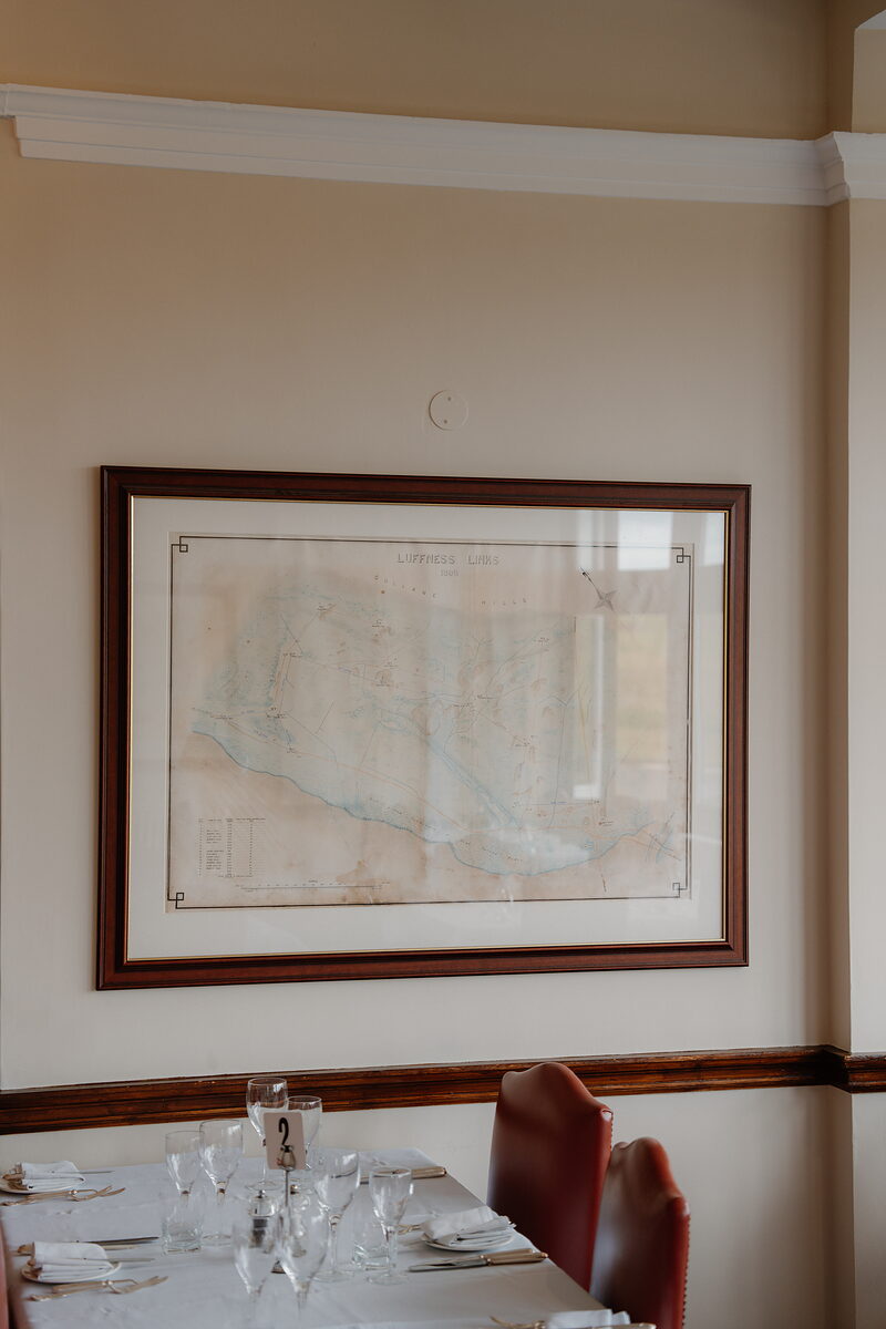 A framed antique map of Luffness Links hanging above a dining table set for two