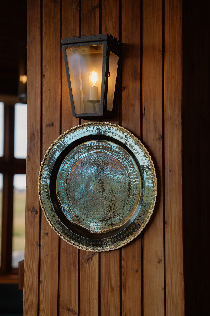 A brass tray mounted beneath a lit wall lantern on a timber-panelled clubhouse wall