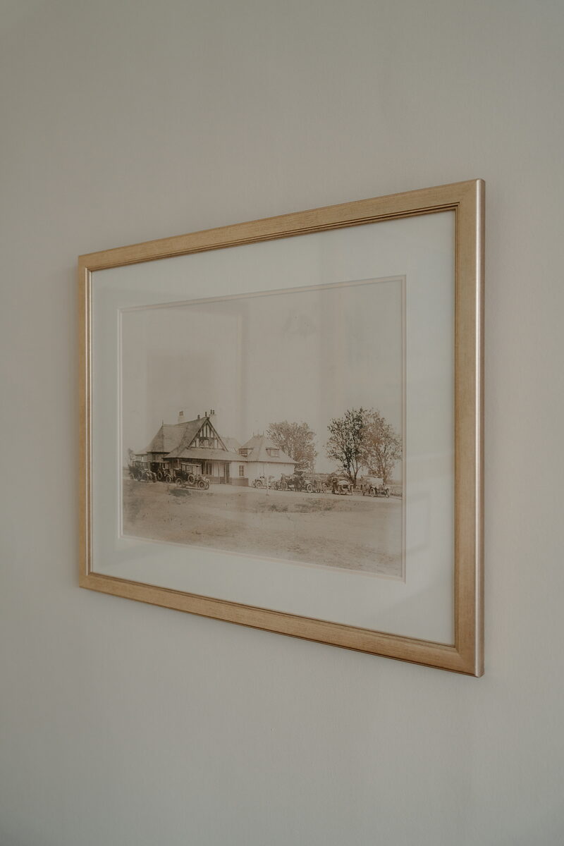 A framed sepia photograph of a clubhouse and parked cars, hung on a plain wall