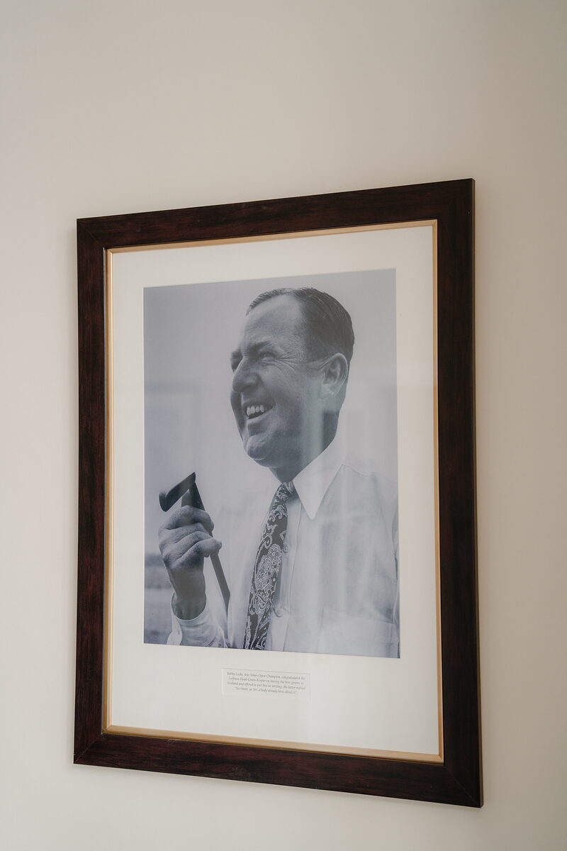 A framed black and white portrait of a laughing man holding a pipe, hung on a plain wall