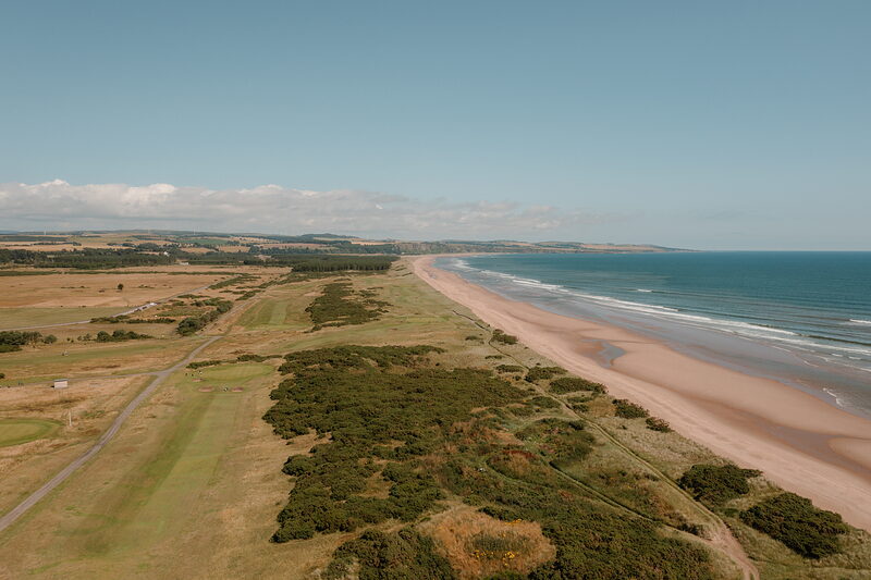 A sandy beach and links course running along the coastline as far as the horizon.