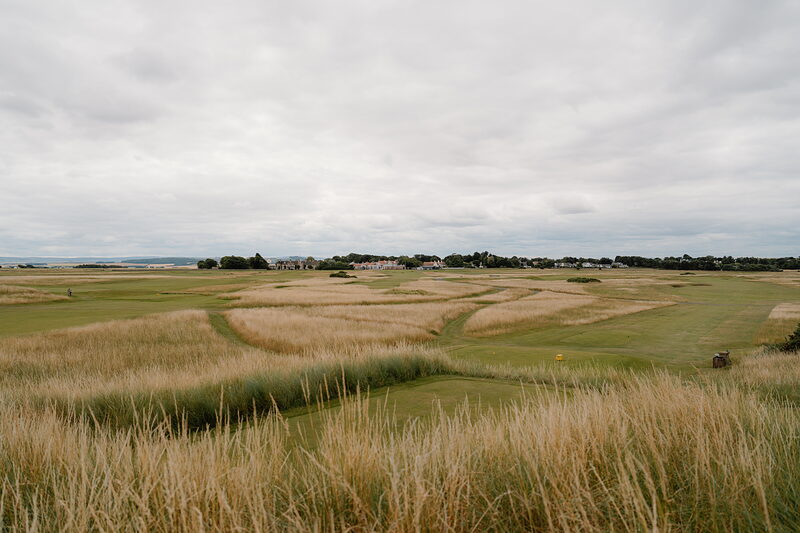 Undulating links fairways bordered by dune grass, a village rising in the distance.