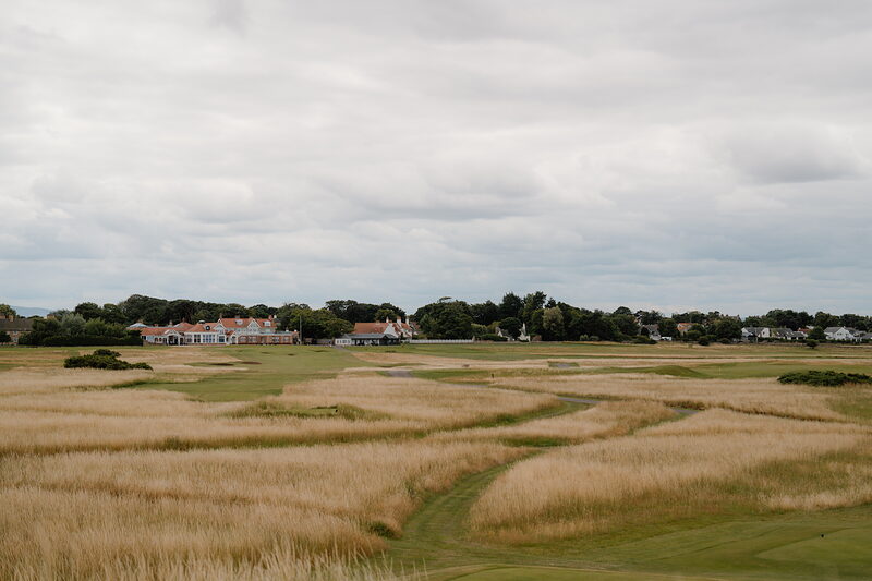 Cottages and trees rising beyond golden dune grass on a links fairway