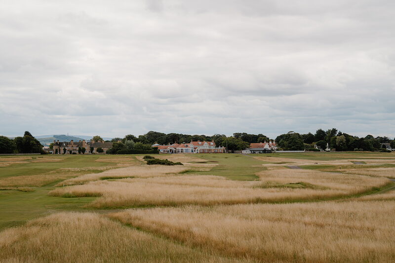 Cottages and trees rising beyond golden dune grass bordering a links fairway