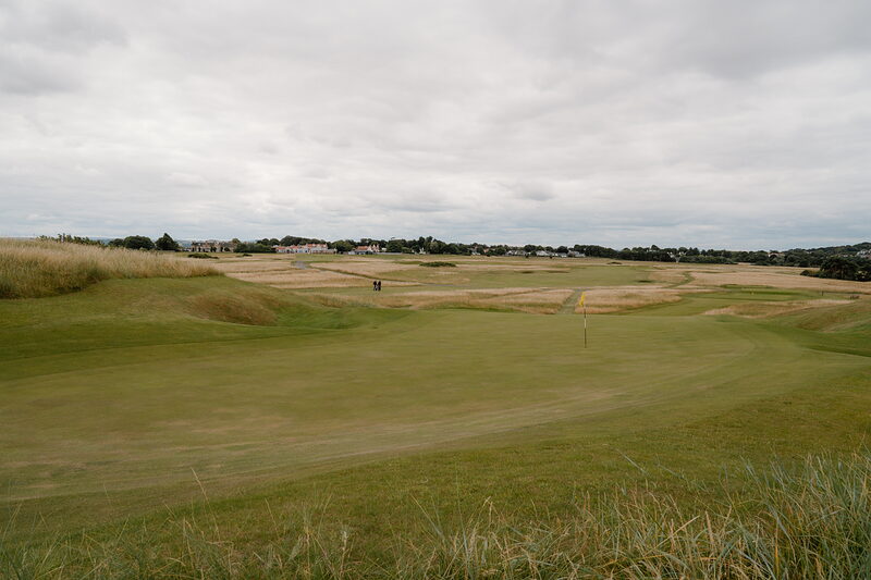 A green bordered by dune grass, a village visible on the horizon across the fairway