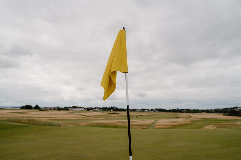 A yellow flag fluttering on a green, a village visible on the horizon beyond the fairway