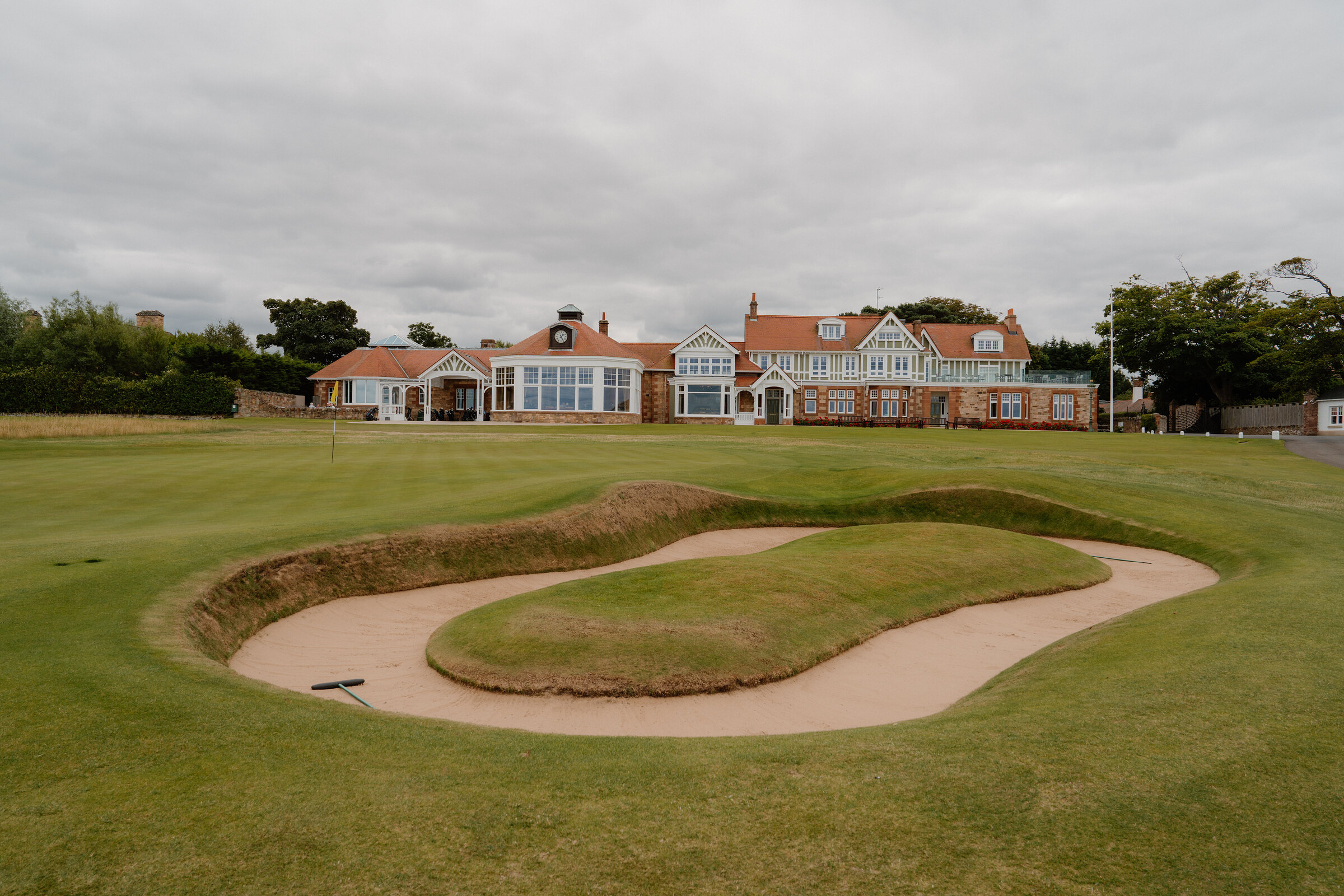 A pair of curved bunkers before a half-timbered clubhouse with red sandstone chimneys