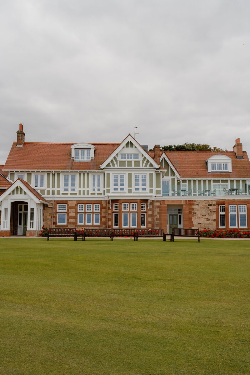 A half-timbered clubhouse facade with sandstone bay windows and wooden benches set on the lawn
