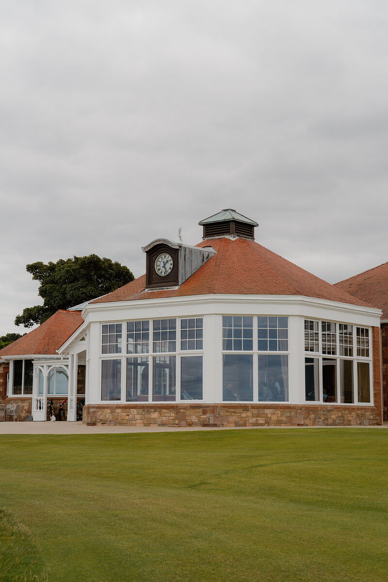 A clubhouse clock tower and conservatory with tall windows overlooking a lawn