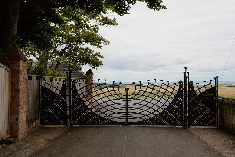 An ornate wrought-iron gate with a fan-shaped crest closing off a driveway